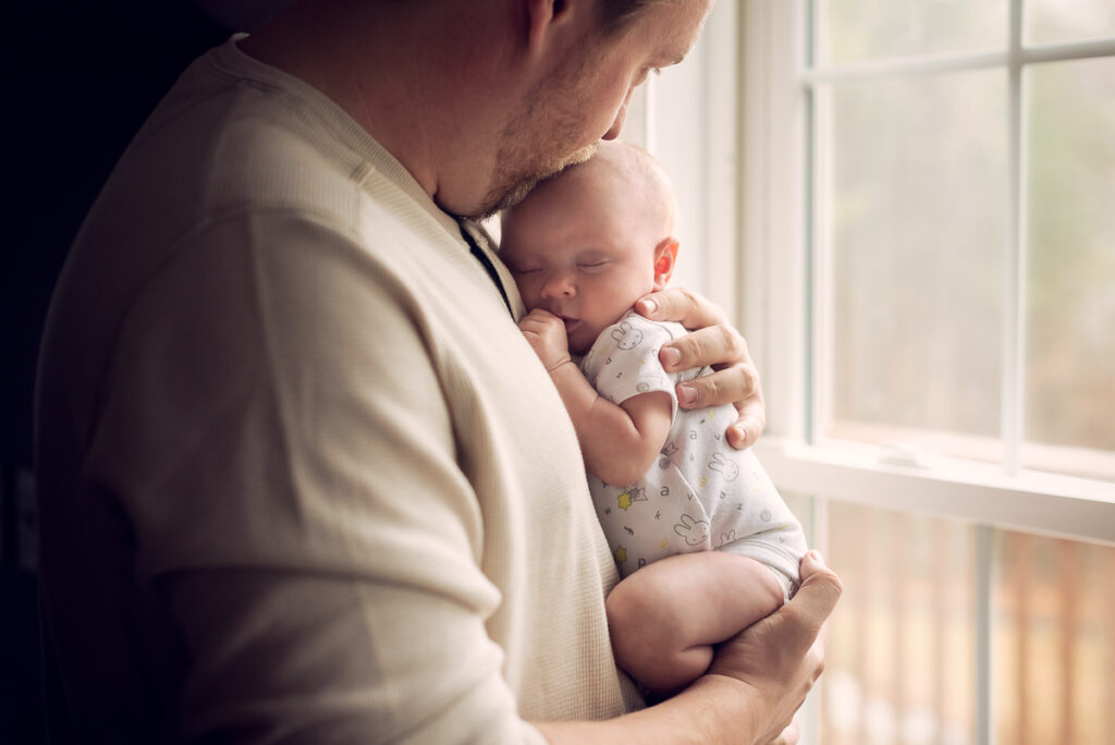 daddy holding baby by home window